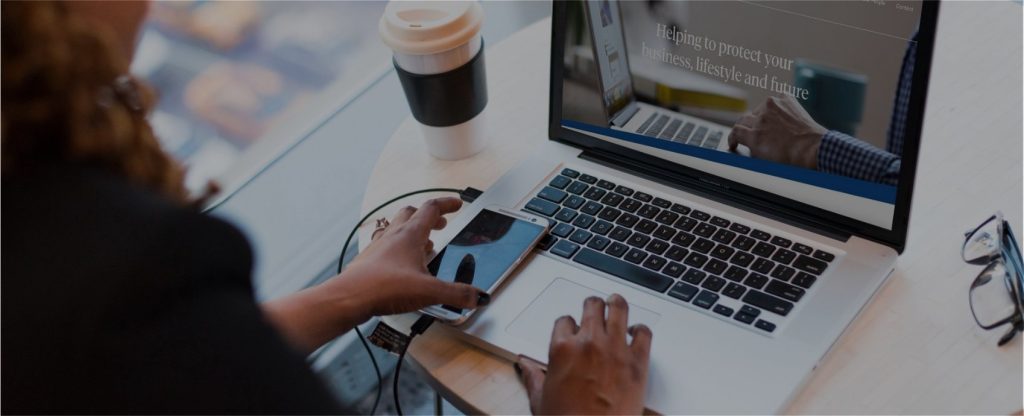 Home Person using a laptop and smartphone at a desk with glasses and a coffee cup nearby